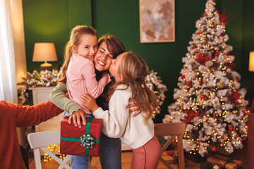 Mother hugging daughters after getting Christmas present over Christmas family dinner at home