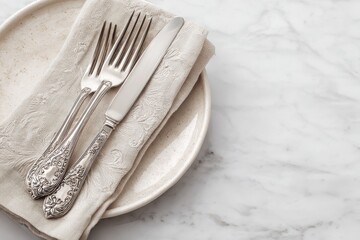 Elegant place setting ornate silver fork and knife rest on a linen napkin atop a beige plate on a marble surface
