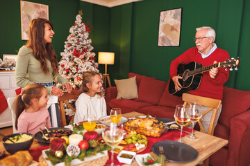 Family playing the guitar and singing Christmas songs while having Christmas dinner together at home