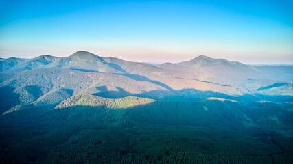 Breathtaking aerial view of mountain landscape at sunset. Golden light bathes rolling hills and lush forests, creating serene and idyllic scene. Distant mountains adding depth to picturesque vista.