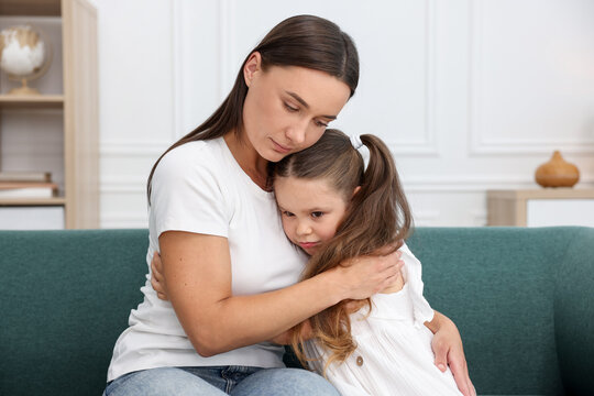 Mother supporting and hugging her sad daughter on sofa at home