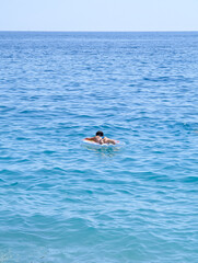 A lone person relaxes on an inflatable ring, peacefully floating in the calm, vast blue sea on a...