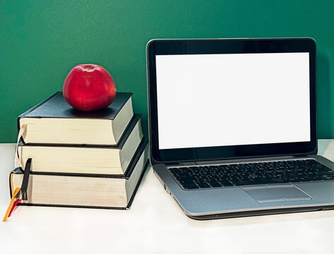 A stack of three books with a red apple on top, next to a laptop with a blank screen. The background is a solid green 