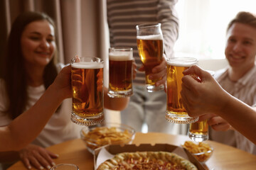 Group of happy friends clinking glasses of beer at table indoors, selective focus
