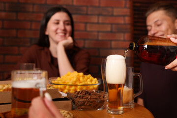 Woman pouring beer into glass at wooden table indoors, selective focus