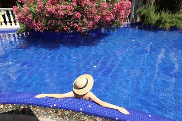 Girl with straw hat in swimming pool outdoors on sunny day, above view