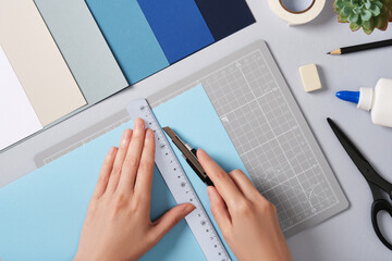 Hands cutting blue paper with ruler and knife on a cutting mat. Concept of craft paper art.