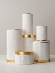 Five white cylindrical forms, textured, with gold rims, varying heights and diameters, arranged on a neutral background