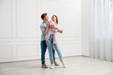 Happy couple dancing together near white wall at home