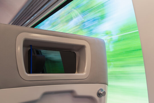 A smartphone rests in a seat-back holder on a high-speed train, with a motion-blurred green landscape rushing past.