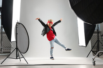 Little boy on light grey background in photo studio with professional equipment