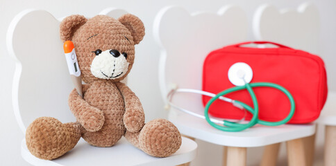 Pediatrician concept. Toy bear, thermometer, medical bag and stethoscope on chairs in clinic
