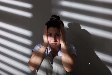 Emotional woman suffering from panic attack near wall indoors