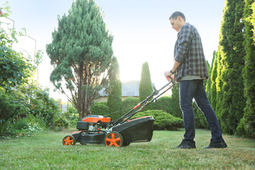 Man cutting green grass with lawn mower in garden