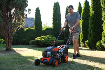 Man cutting green grass with lawn mower in garden