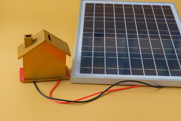 Composition with solar panel and model house on background.
