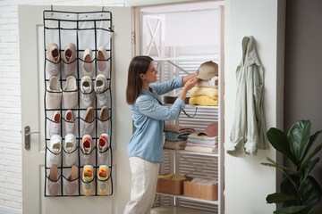 Woman taking cap from shelf near organizer with different footwear at home. Shoe storage