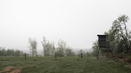 Hunting stand on misty meadow edge in quiet rural countryside at dawn