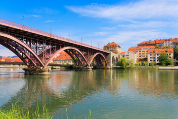 A vibrant view of the iconic bridge in Maribor, Slovenia, showcasing its striking architecture and nearby historic buildings along the river.