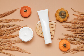 Mockup tube of facial, hand cream or body lotion on ceramic stand with pampas grass and pumpkins. Autumn skincare, top view