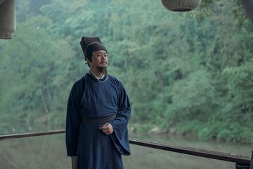 A man in traditional attire stands by a serene riverside.