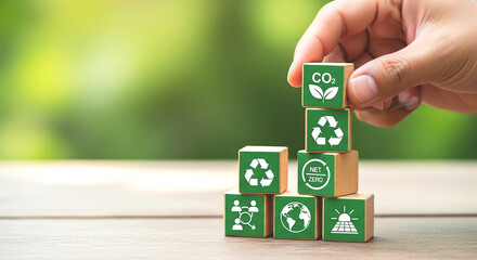 Hand stacking wooden blocks with environmental icons on a wooden surface with green background bokeh