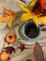 Cup of tea with autumn leaves and pomegranates on warm sweater. Cozy autumn mood and relaxation concept. Top view, flat lay. Warm, peaceful, and homey atmosphere. Autumn composition. 