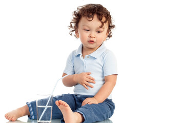 Cute curly haired toddler drinking water in a glas form a straw on white background with a happy smile