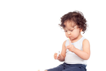 Curly haired toddler brushing teeth with toothbrush and holding toothpaste
