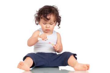 Curly haired toddler brushing teeth with toothbrush and holding toothpaste
