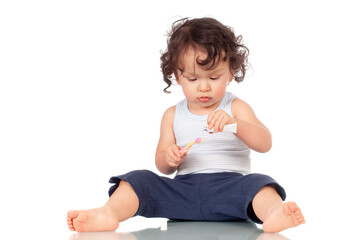 Curly haired toddler brushing teeth with toothbrush and holding toothpaste