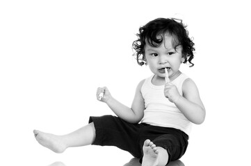 Curly haired toddler brushing teeth with toothbrush and holding toothpaste