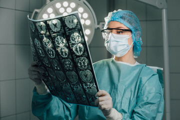 Female surgeon in scrubs and surgical cap, examining medical imaging in operating room, illuminated...