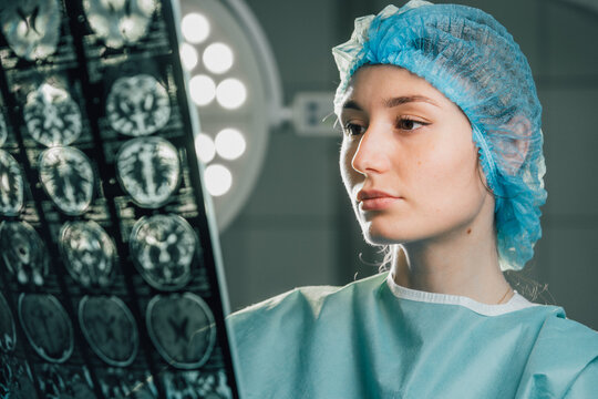 Female surgeon in operating room, wearing surgical cap and gown, examining brain scan images under bright surgical lights, showcasing dedication to patient care and medical expertise - Powered by Adobe