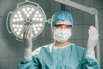Surgeon in sterile surgical attire, wearing gloves and mask, preparing for operation in modern...