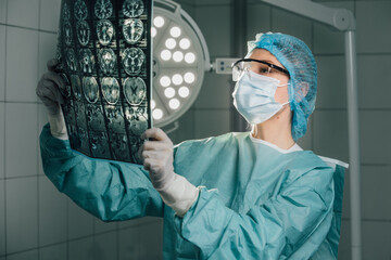 Surgeon in green scrubs and protective gear, examining medical imaging in an operating room,...