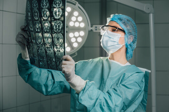 Surgeon in green scrubs and protective gear, examining medical imaging in an operating room, illuminated by bright surgical lights, showcasing the importance of diagnostics in healthcare