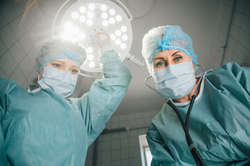 Two female surgeons in scrubs and masks, preparing for a surgical procedure under bright operating...