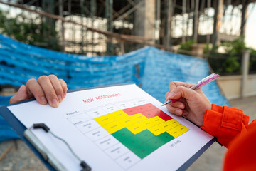 Action of a project manager is writing on risk assessment matrix form to rating the risk of house...