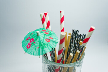 Clear glass with mixed drinking straws and green floral cocktail umbrella