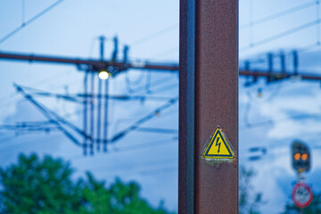 Rusty pole with electric warning sign and railway structures