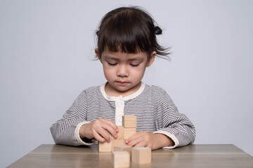 A focused child builds with wooden blocks on a table, showcasing creativity and concentration in a minimalistic setting.