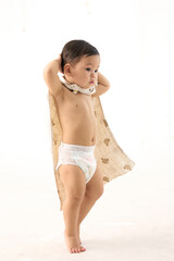 Toddler boy wrapped in blanket, bending forward playfully, white background