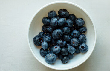 Bowl of blueberries is shown in a white bowl. The blueberries are fresh and ripe, and they are arranged in a way that makes them look like a small, colorful pile