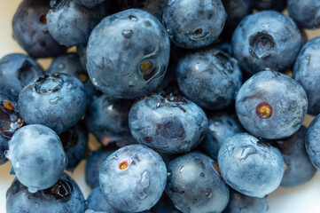 Close up of blueberries in a bowl. The blueberries are fresh and plump, with a shiny surface. The bowl is white, and the blueberries are scattered throughout the bowl, creating a visually appealing