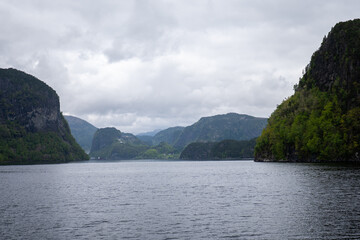 Scenic overlook of a tranquil fjord surrounded by lush green mountains on a cloudy day in Norway...