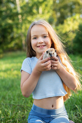 Blonde caucasian young girl smiling holding hedgehog in park. Child bonding with exotic pet hedgehog