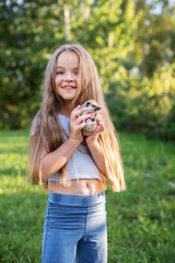 Caucasian young girl holding a hedgehog outdoors in sunny park. Child caring for African pygmy hedgehog