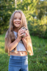 Young caucasian girl smiling and holding a hedgehog outdoors in sunlit garden
