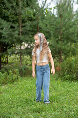 Young caucasian girl with long hair in blue pants standing outdoors in green park